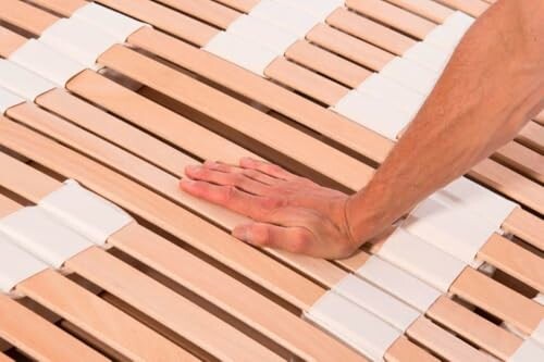 Hand drückt auf Holzbettlatten.