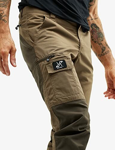 Nahaufnahme von Herren-Outdoor-Hose mit Taschen und Tattoos auf den Armen.